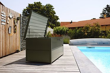 Le coffre de jardin anthracite se trouve sur une terrasse à côté d'une grande piscine