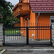 Portail à double battant avec barres noires en aluminium sur clôture à barres autour d'une maison orange