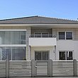 Clôture à lamelles couleur argent avec portillon de jardin devant une maison à deux niveaux en blanc et gris