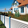 Gartenzaun mit weißen Lamellen und blauen Zaunpfosten unrahmt ein Haus im Stil der 90er mit blauen Fensterrahmen