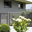 Portillon de jardin avec élément de clôture à lamelles en aluminium couleur gris noble avec des buissons devant