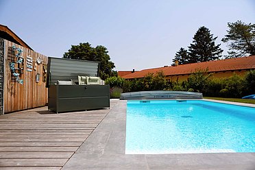 Le coffre de jardin anthracite est ouvert à côté d'une grande piscine 