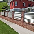 weißer Gartenzaun mit Lamellen auf Mauersockkel aus Backsteinen umzäunt ein Appartmenthaus in den Bergen