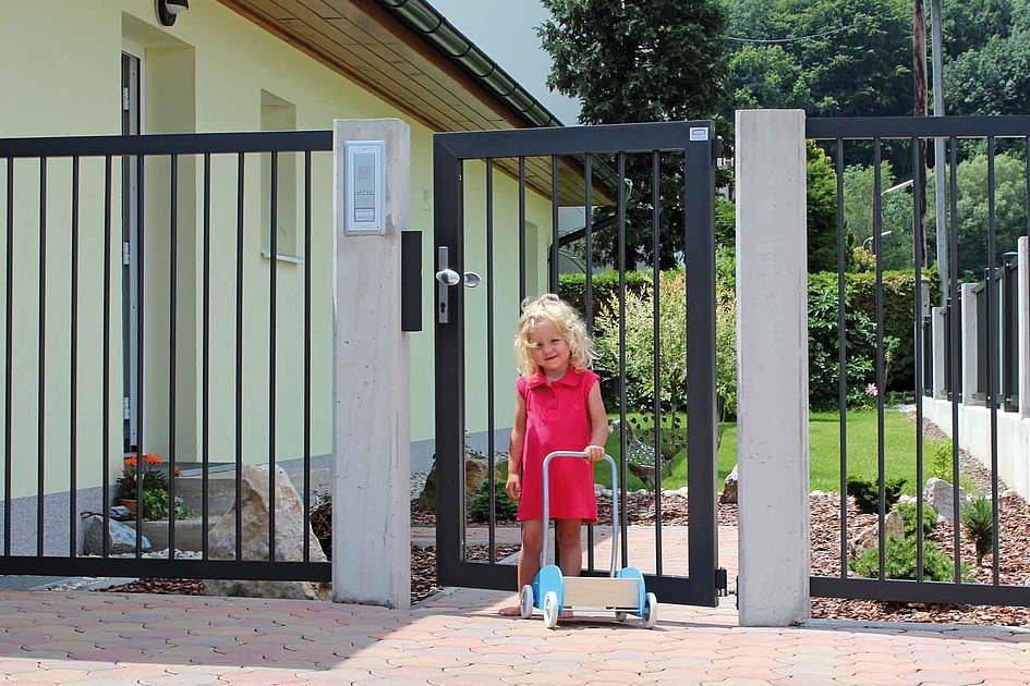 petite fille tenant une trottinette devant un portillon de jardin couleur anthracite doté de barres rondes simples 