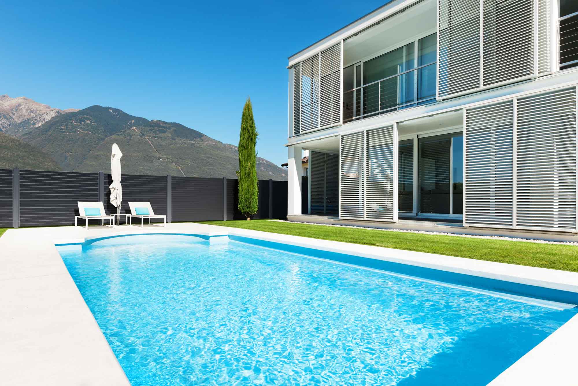 maison moderne avec piscine dans le jardin et vue sur les montagnes, entourée d'une clôture en aluminium